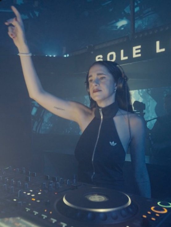 Sole DJing with her arm raised, her name on the screen behind her