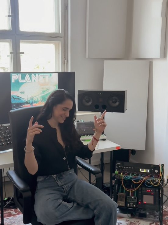 Sole dancing in her studio chair, the Planet 3 cover on the screen behind her