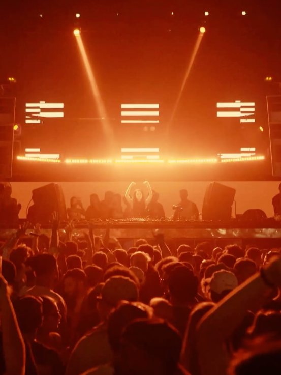 Sole in the booth at INPUT, arms raised under orange lights